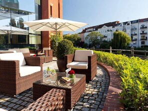 An outdoor seating area with wicker furniture, a glass table, and a large umbrella. - Abion Villa Suites (Berlin)