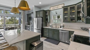 A modern kitchen with green cabinets, a marble island, stainless steel appliances, and pendant lighting.