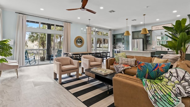 A spacious living area with a large window, a ceiling fan, and a kitchen in the background.