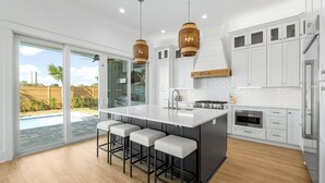 A modern kitchen with a large island, white cabinets, and a view of a backyard. - Tango Vista With Pool, Elevator, And Beach Views (Miramar Beach)
