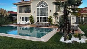 A large house with a swimming pool, a patio with furniture, and a well-maintained garden. - Lüks villa (İstanbul)