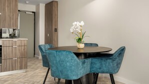 Een moderne eetruimte met een ronde tafel, stoelen bekleed met blauwgroen en een vaas met witte bloemen.