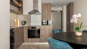 Een moderne keuken met houten kastjes, een inbouwoven en een eethoek met een ronde tafel en blauwe stoelen.