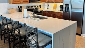 Una cocina moderna con armarios de madera, electrodomésticos de acero inoxidable y una isla de mármol con taburetes de bar.