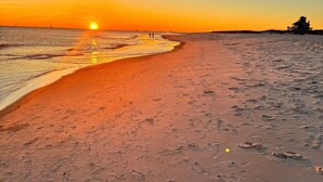Una playa al atardecer con huellas en la arena y una estructura a lo lejos.