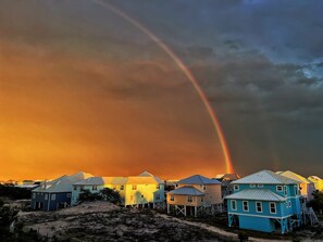 Una propiedad frente a la playa con casas elevadas sobre pilotes, una playa de arena y un arcoíris en el cielo.