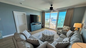 Una sala de estar moderna con un conjunto de sofás, una mesa de centro, un televisor y vistas de un paisaje urbano a través de amplios ventanales.