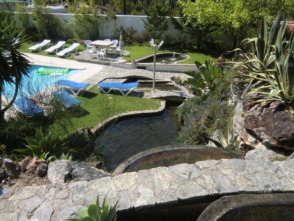 A swimming pool with lounge chairs, a small waterfall, and surrounding greenery.