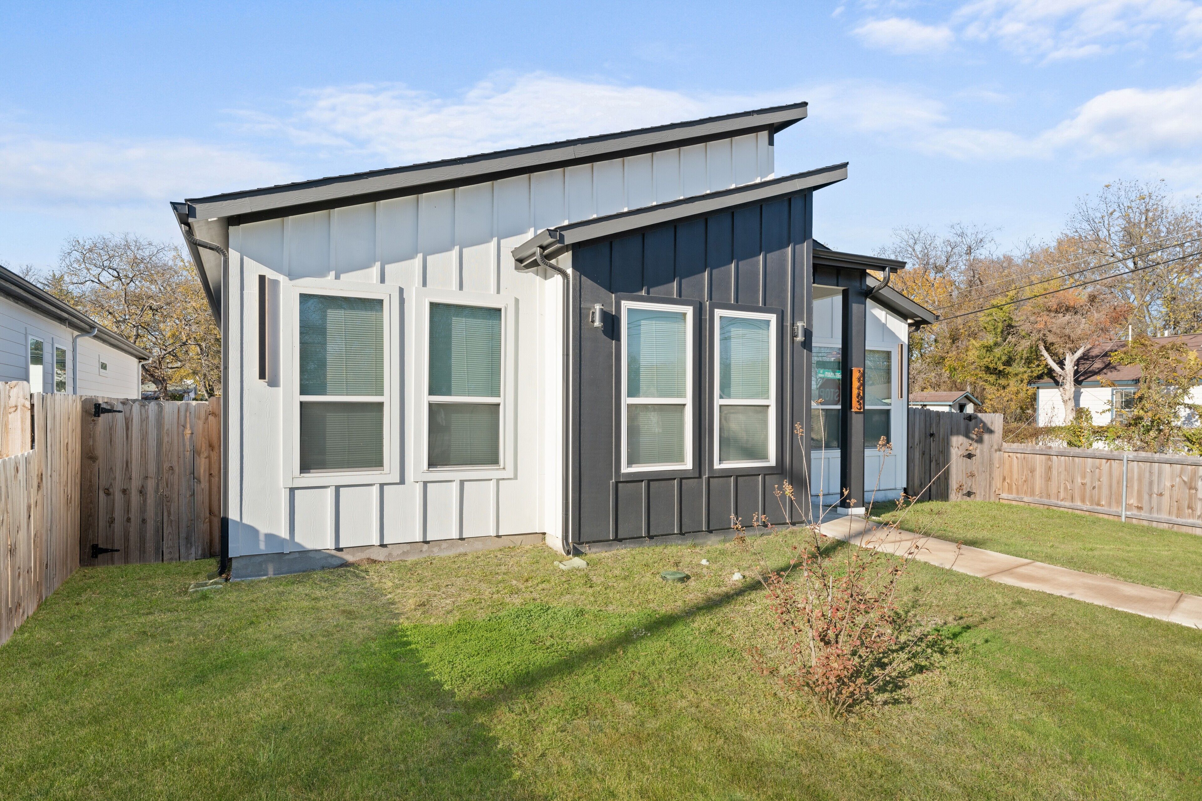 A modern single-story house with a sloped roof, large windows, and a fenced backyard.