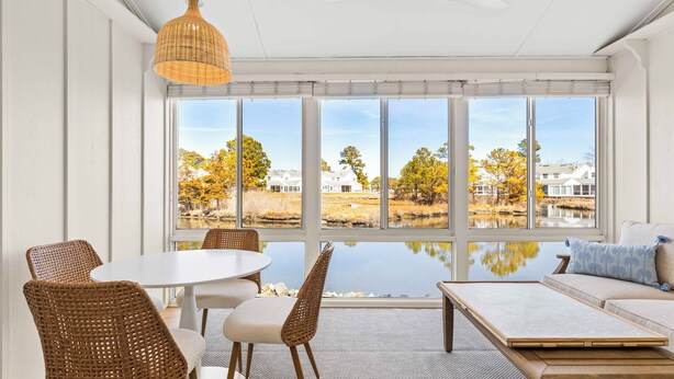 A room with large windows, wicker furniture, and a view of a lake and trees. - NEWLY RENOVATED - Mallard Lakes - Rare 3 bedroom unit near Fenwick & OC. (Selbyville)
