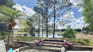 An outdoor patio with white chairs, a stone pathway, and a view of a lake with trees and a cloudy sky. - Waterview 3 bed in Sunridge Woods (Davenport)