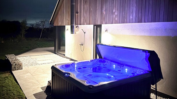 A hot tub with a blue light, located outside a building with a wooden exterior.