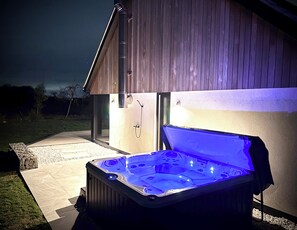 A hot tub with a blue light, located outside a building with a wooden exterior. - Studio Apartment bordering the Ickworth Estate, Pet-Friendly, 5 minutes to Bury! (Bury St Edmunds)
