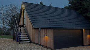 A modern building with a sloped roof, a wooden exterior, and a gravel driveway.