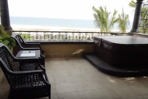 Un balcón con vista al océano, una silla de metal negro y una mesita.