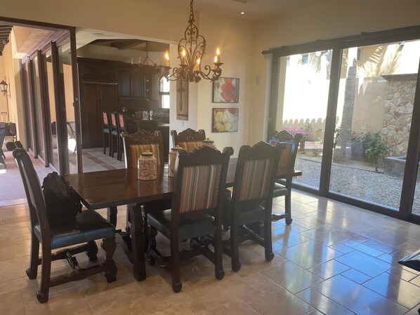 A dining area with a large table and chairs, a chandelier, and a view of the outdoor patio through large sliding doors.