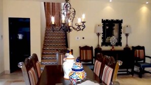 A dining area with a large wooden table, striped upholstered chairs, a chandelier, and a staircase in the background. - Novaispania Pueblo Bonito Sunset Beach (Cabo San Lucas)