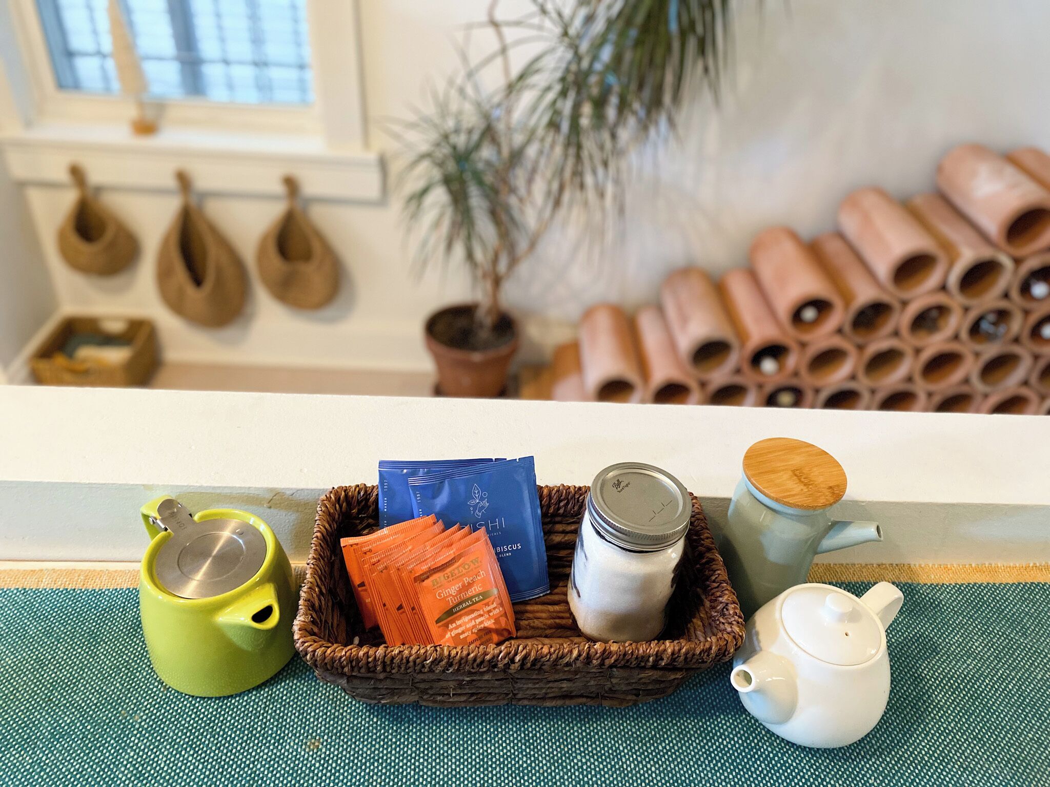 A wicker basket containing tea bags, a jar of sugar, and a teapot on a table.