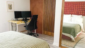 A bedroom with a bed, a desk with two monitors, a chair, a wooden panel wall, and a mirror reflecting the bed and a patterned headboard. - Peaceful Living-2Bdrm/2Bath w/Private Parking, WiFi-Work Station-Wicker Park! (Chicago)