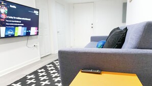 A modern living room with a grey sofa, a yellow side table, and a flat-screen TV displaying a streaming service. - Peaceful Living-2Bdrm/2Bath w/Private Parking, WiFi-Work Station-Wicker Park! (Chicago)