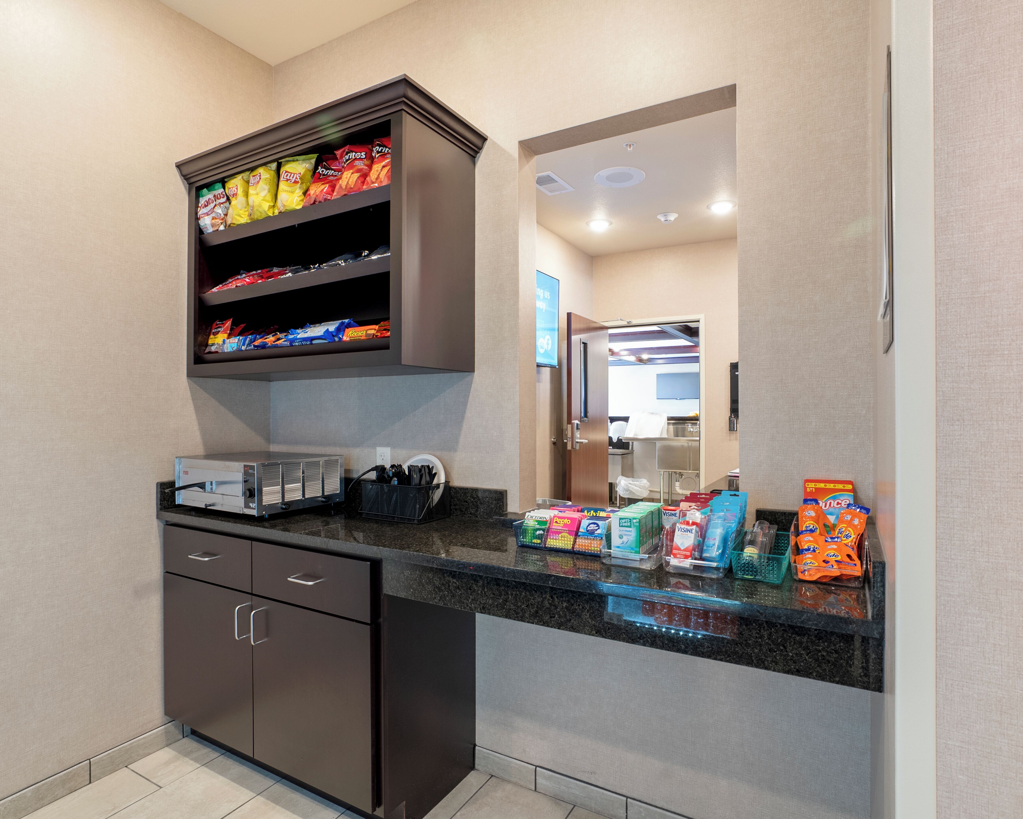A modern kitchen with a built-in microwave, a coffee machine, and a variety of snacks and condiments on the counter.
