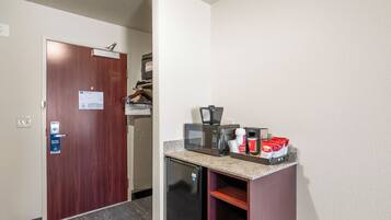 A compact kitchenette with a microwave, coffee maker, and storage for coffee pods.