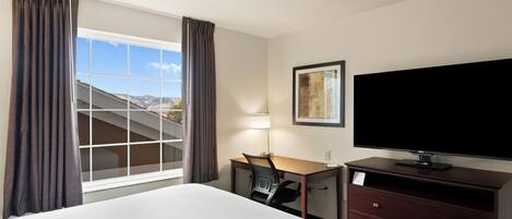 Quarto de hotel com uma cama grande, uma escrivaninha, televisão e janela com cortinas.