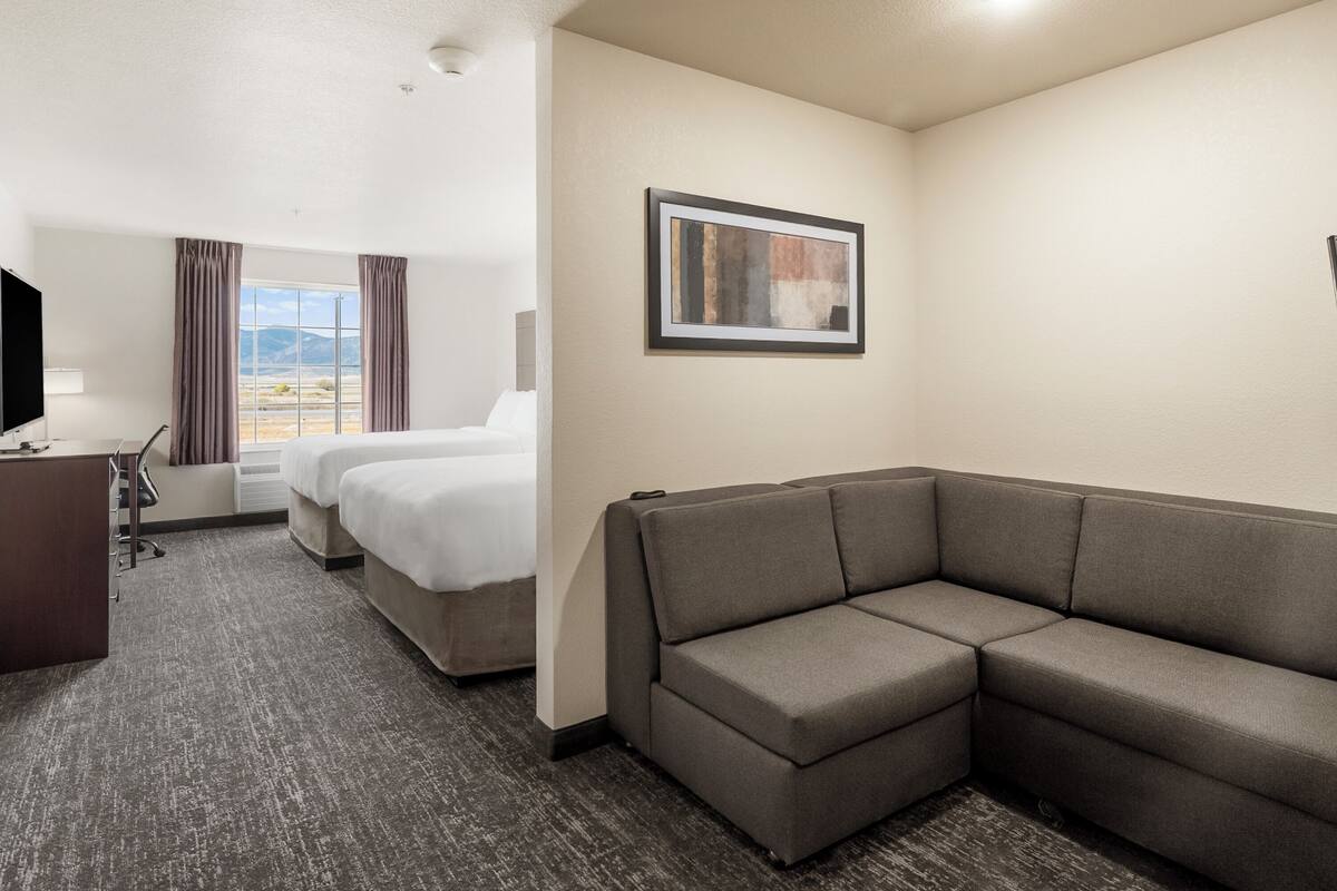 A hotel room with a large bed, a sofa, a desk with a chair, a TV, and a window with curtains.