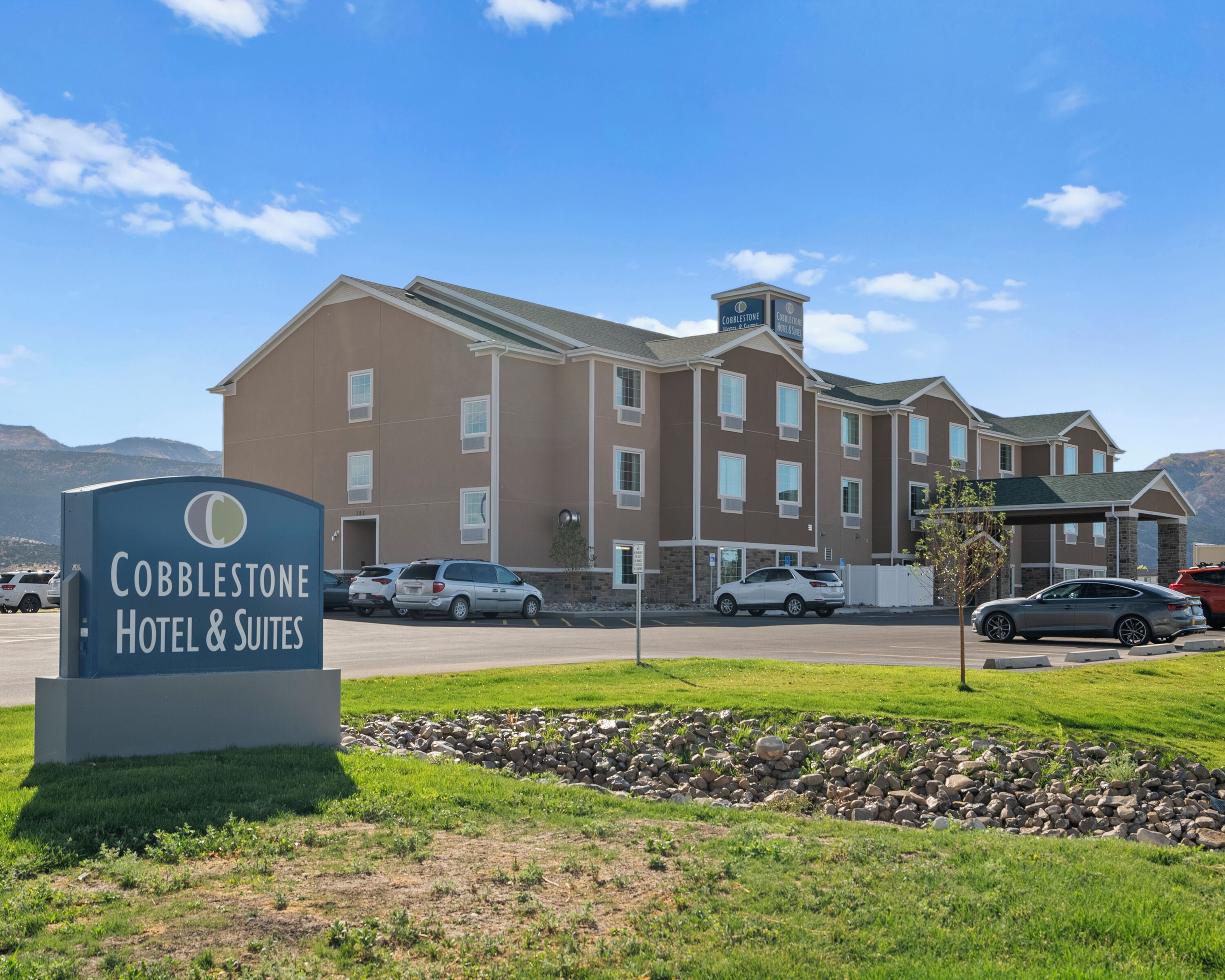 Une enseigne d’hôtel indiquant « Cobblestone Hotel & Suites », et un bâtiment doté de nombreuses fenêtres et d’une façade en pierre.
