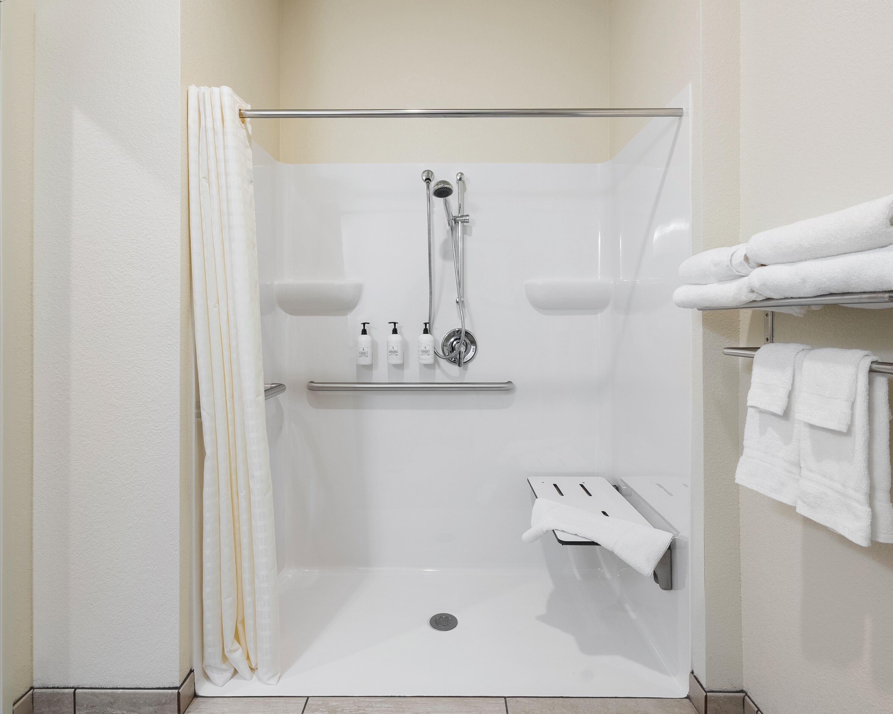 Une cabine de douche moderne avec une porte en verre, un porte-serviettes avec des serviettes pliées et une étagère contenant des articles de toilette.