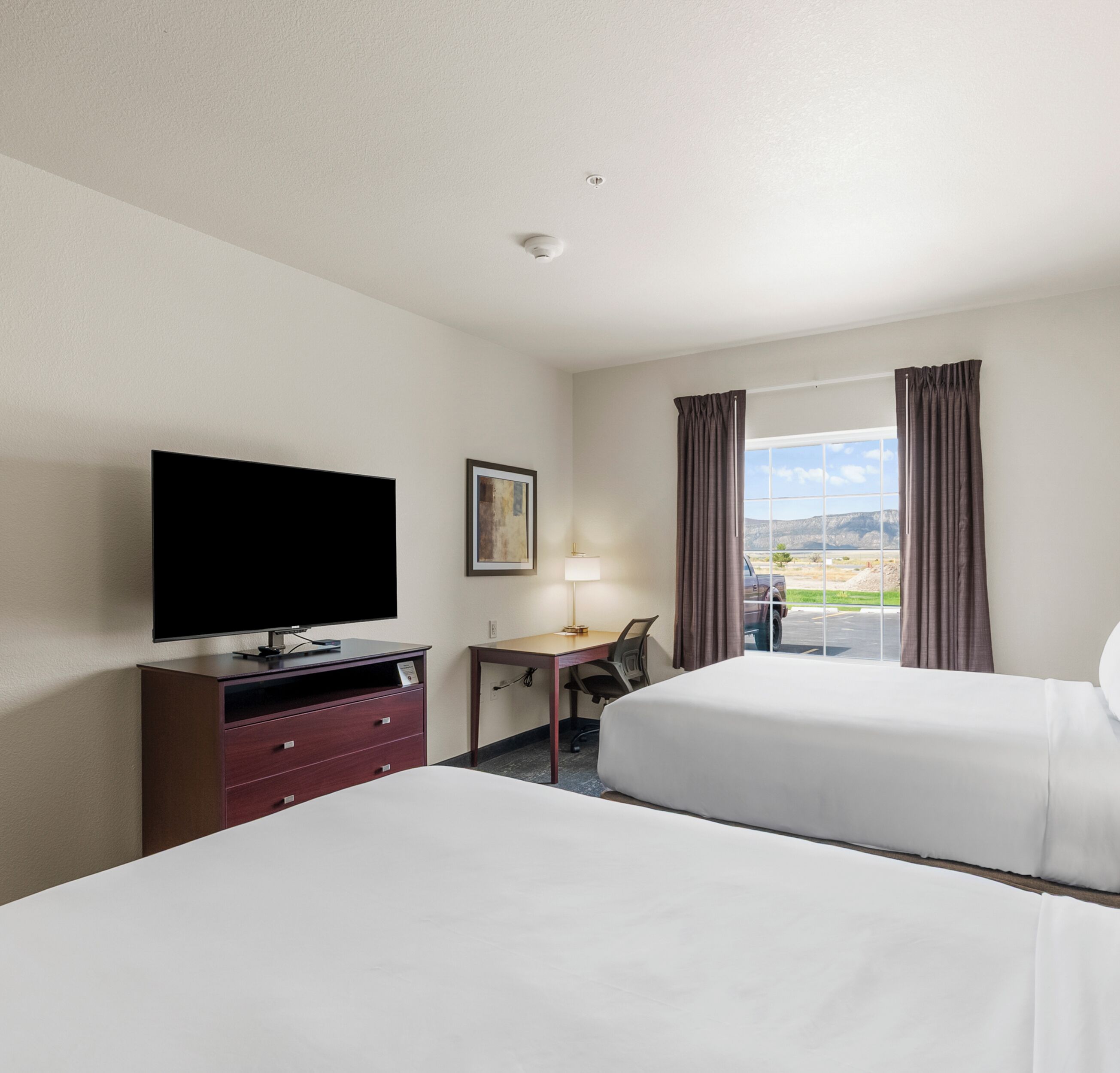 Habitación de hotel con dos camas, un escritorio, un televisor y una ventana con cortinas.