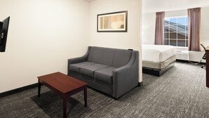 A hotel room with a gray sofa, a wooden table, a bed, and a window with curtains. - Cobblestone Hotel & Suites - Ephraim (Ephraim)