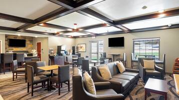 A hotel lobby with a seating area, a kitchen, and a large window offering a view.