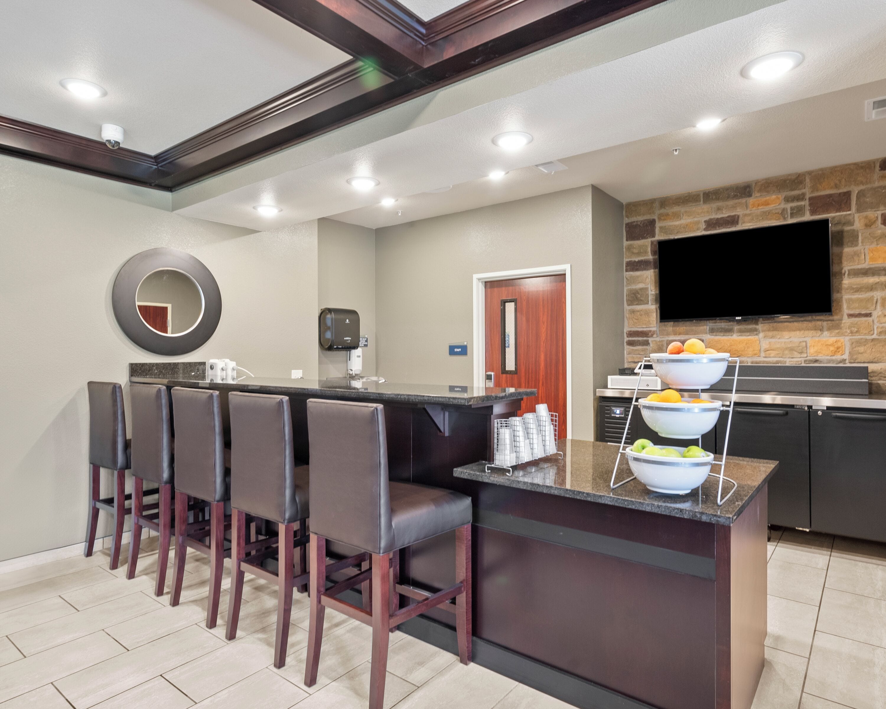 A modern kitchen with a stone backsplash, a flat-screen TV, and a bar area with stools.