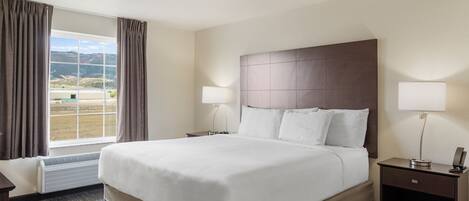 Habitación de hotel con una cama grande, dos mesitas de noche, un ventanal con cortinas y vistas al exterior.