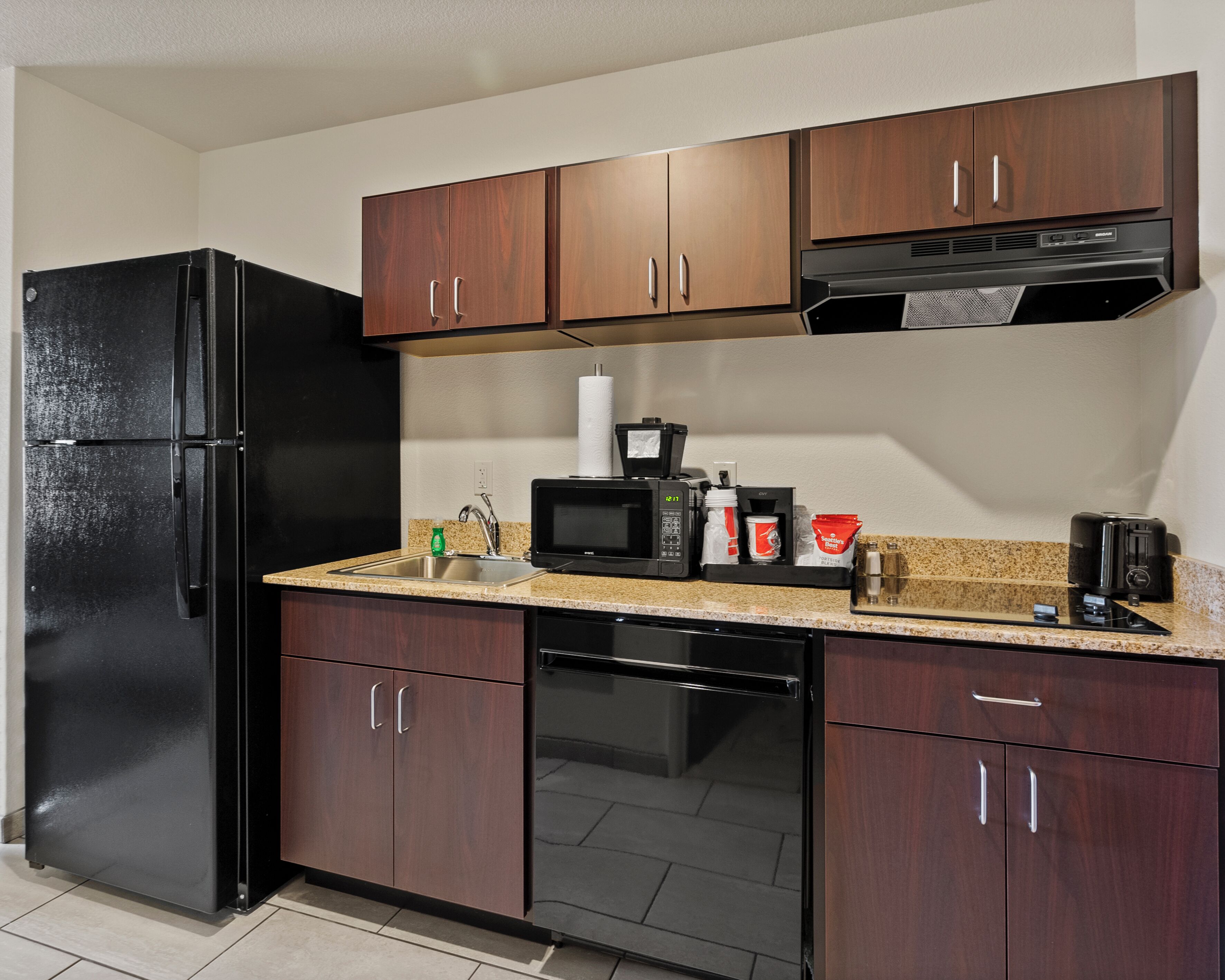 A compact kitchen with a black refrigerator, a microwave, a coffee maker, and a toaster.