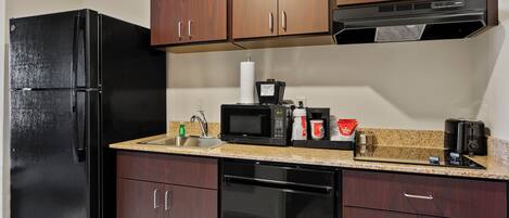 A compact kitchen with a black refrigerator, a microwave, a coffee maker, and a toaster.