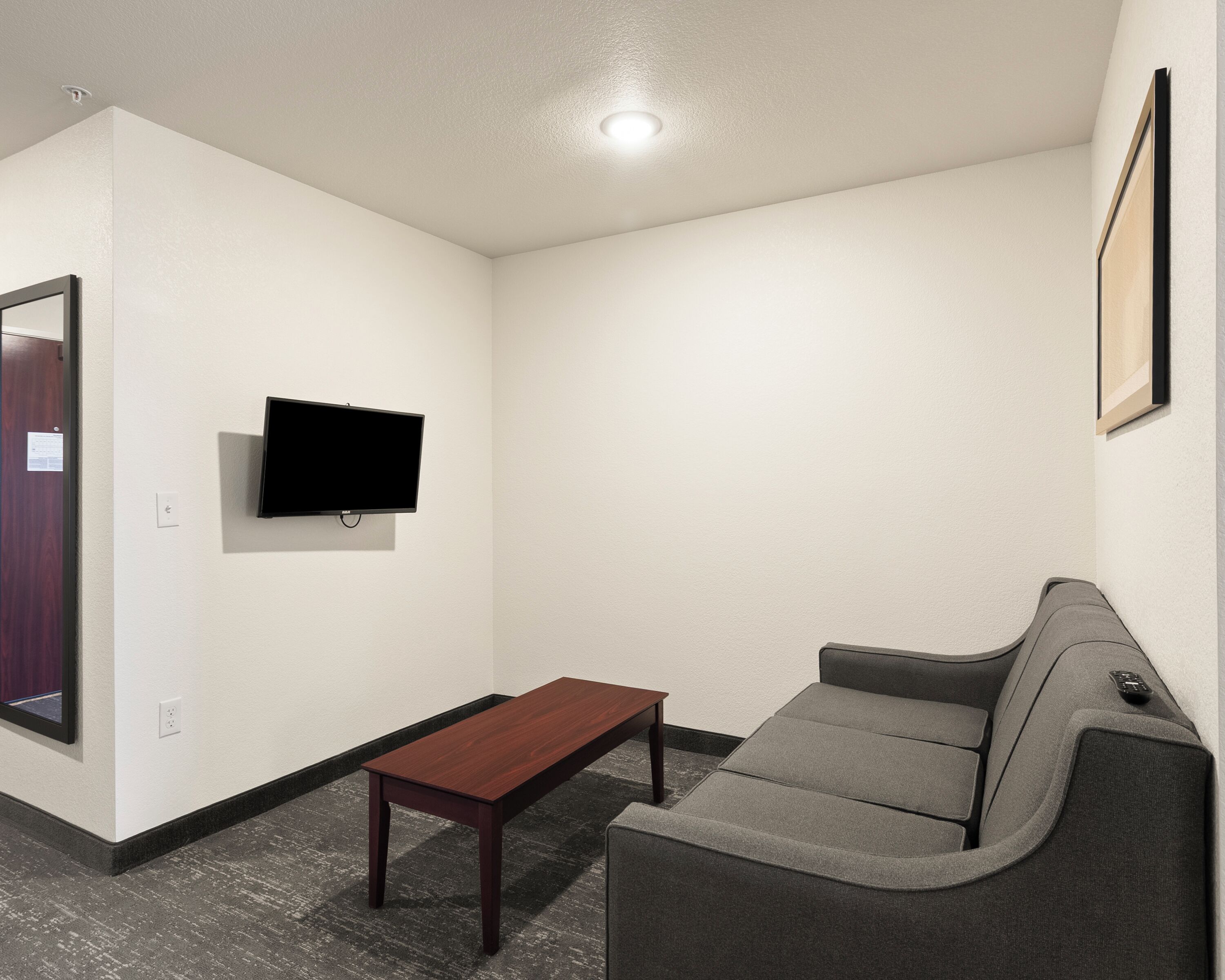 A room with a flat-screen TV mounted on the wall, a wooden coffee table, and a gray sofa.