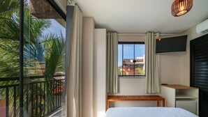A hotel room with a bed, a TV, a desk, and a window with curtains. - Suíte 8 Ala pôr sol Residencial Solavir (Bombinhas)
