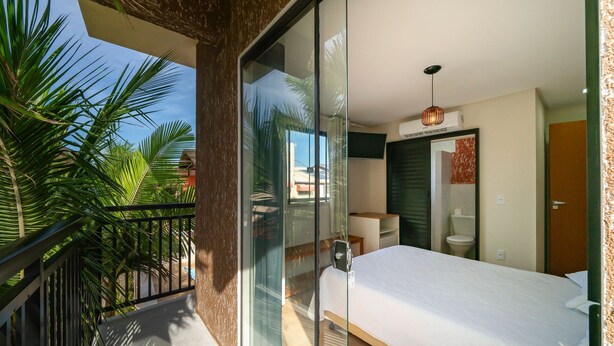 A modern bedroom with a large bed, a balcony with a glass door, and a view of palm trees. - Suíte 8 Ala pôr sol Residencial Solavir (Bombinhas)