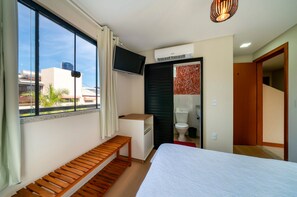 Une chambre d’hôtel avec un lit, un banc en bois, une télévision, un appareil de climatisation et une vue sur les bâtiments environnants.
