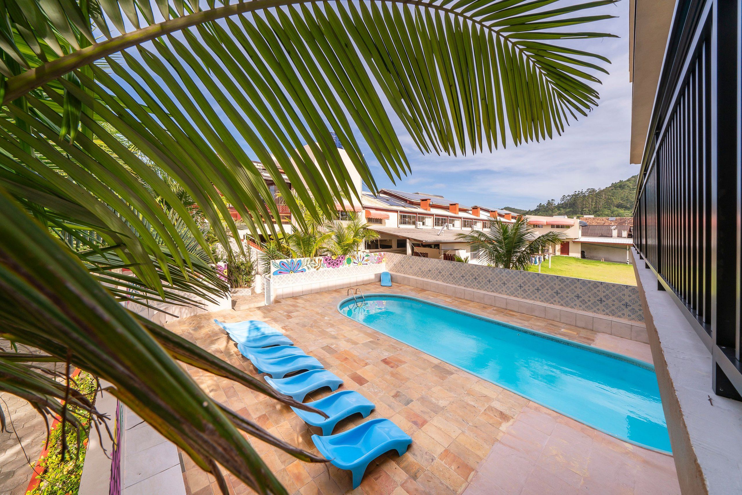 A swimming pool with blue lounge chairs, surrounded by palm trees and a view of buildings in the background.