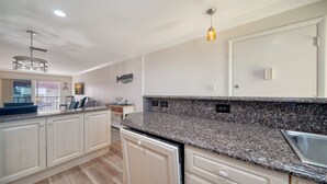 Une cuisine moderne dotée de plans de travail en granit, de meubles blancs et d’un lave-vaisselle encastré.
