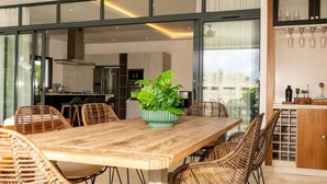 Zona pranzo moderna con tavolo in legno e sedie in vimini, un centrotavola con pianta verde e una cucina sullo sfondo.