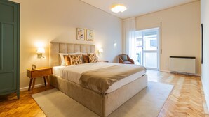 Ein Schlafzimmer mit einem großen Bett, zwei Nachttischlampen, einem Sessel, einem Fenster mit Vorhängen und einer Heizung.
