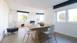 A modern dining area with a wooden table and white chairs, large windows, and a view of trees. - GIL LOVE - Luxurious V5 w/ Pool by LovelyStay (Vila Nova de Gaia)