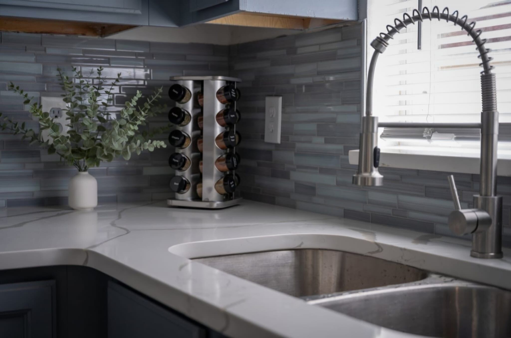 Uma cozinha moderna com uma pia de aço inoxidável, um espaço para vinhos e um vaso com planta.