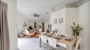 Un comedor con una mesa de madera dispuesta para cuatro personas, sillas blancas y un ventilador de techo.