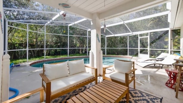Habitación soleada con piscina, muebles de madera y ventanas amplias con vistas a una zona de piscina.