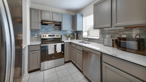 Una cocina moderna con electrodomésticos de acero inoxidable, gabinetes grises y un salpicadero de azulejos.